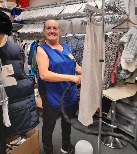 Woman wearing blue Cats Protection vest steaming clothes in a stock room
