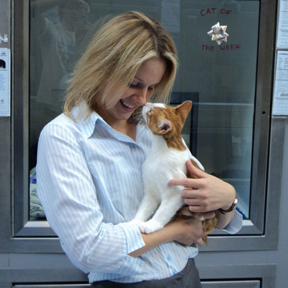 blonde woman holding ginger and white cat while they rub noses