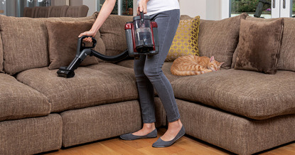 woman hoovering sofa that ginger tabby cat is asleep on