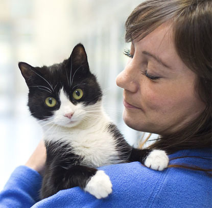 brunette woman in Cats Protection jumper holding a black and white cat