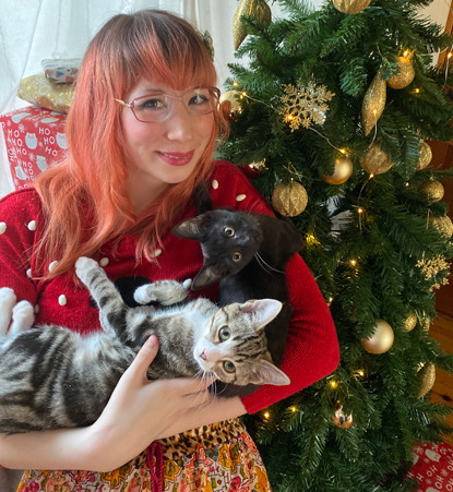 woman in red jumper and glasses holding cats in front of christmas tree