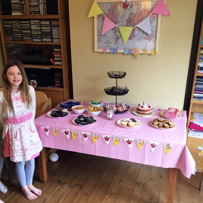 girl standing next to table full of afternoon tea, cakes and biscuits