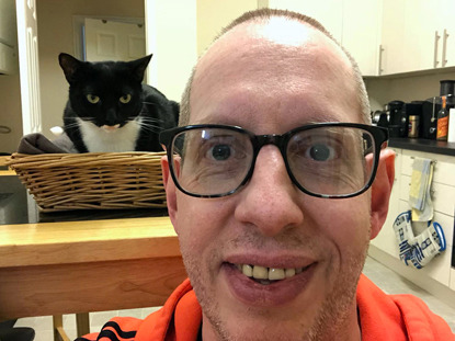 man wearing glasses with black and white cat sat in basket behind him