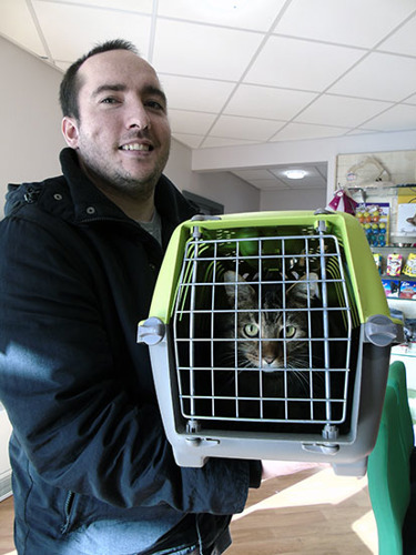 man holding cat carrier containing tabby cat
