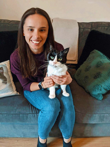 brunette woman on grey sofa holding black and white cat