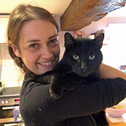 brunette woman holding black cat in kitchen