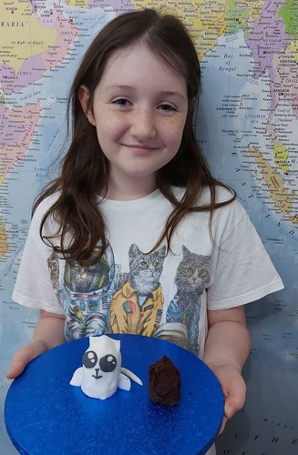 young brunette girl holding plate with rocketship cat cake on it
