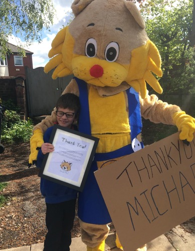 Person in cat mascot costume with arm around young short-haired brunette boy holding thank you certificate