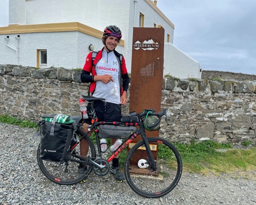 man wearing cycling gear and helmet next to a bike in front of a stone wall