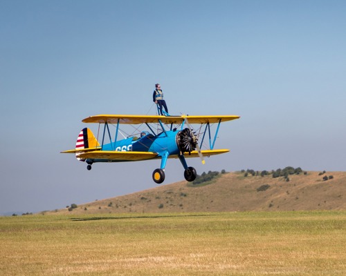 person strapped to top of blue and yellow biplane what's in the air