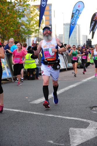 man with long grey beard and wearing running vest and shorts running in a race